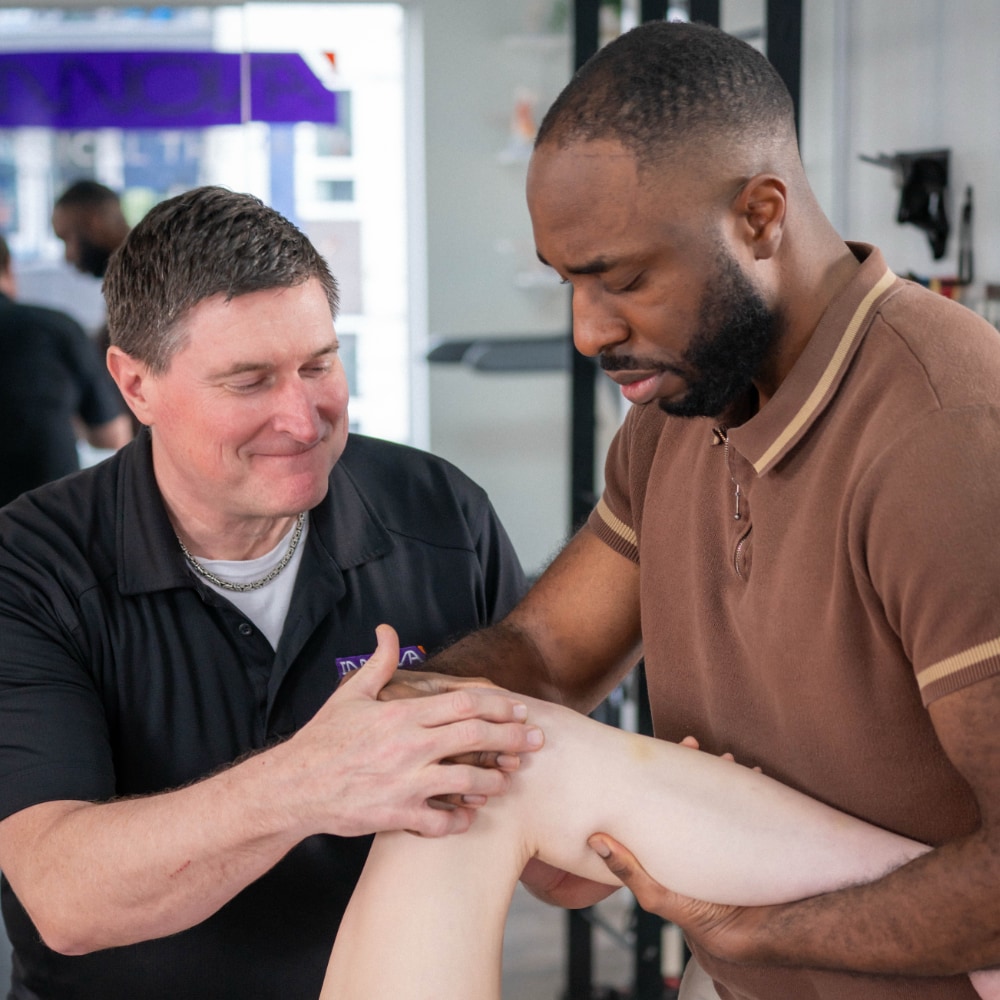 Bret points to an area of a patient's knee while another therapist performs a physical examination of the region