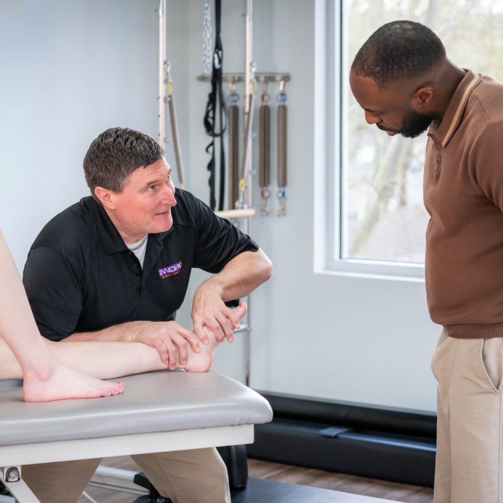 Bret demonstrates a therapy technique on a patient's foot while another therapist observes.