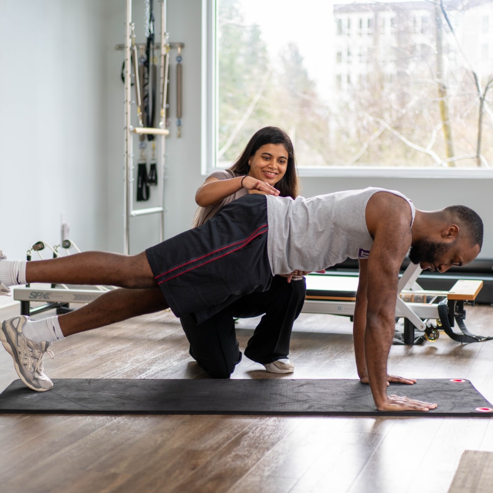 A therapist assists a patient with an extended arm plank