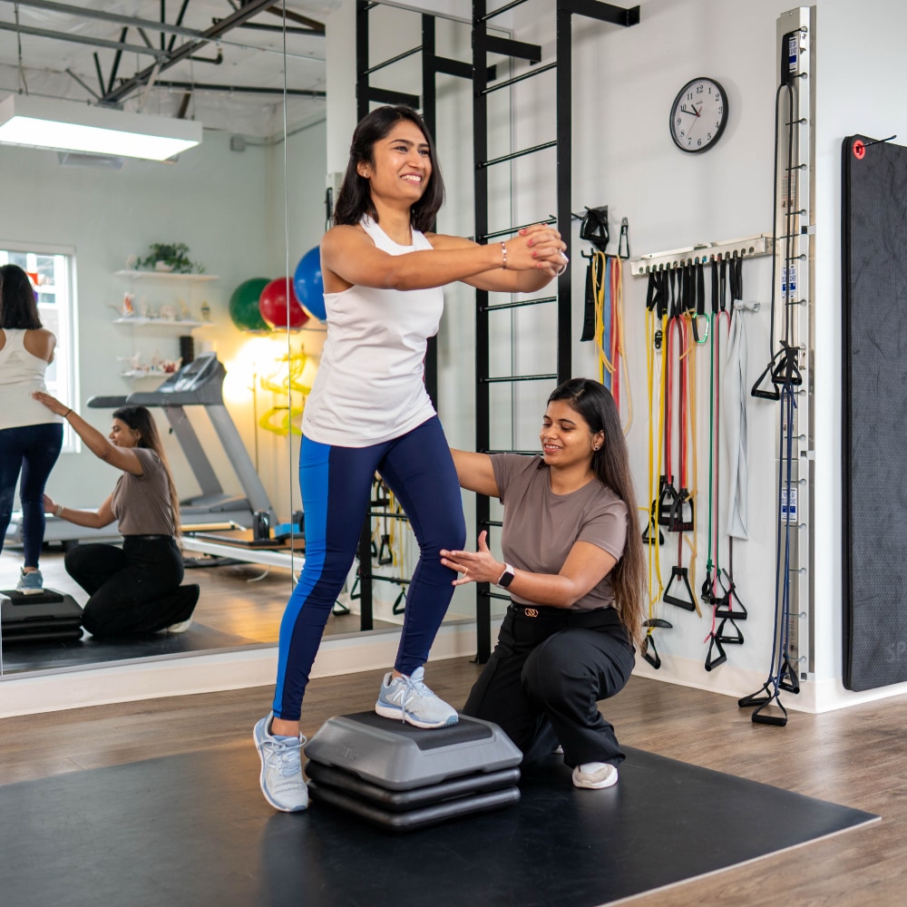 A patient with one leg up on a block is assisted by a therapist